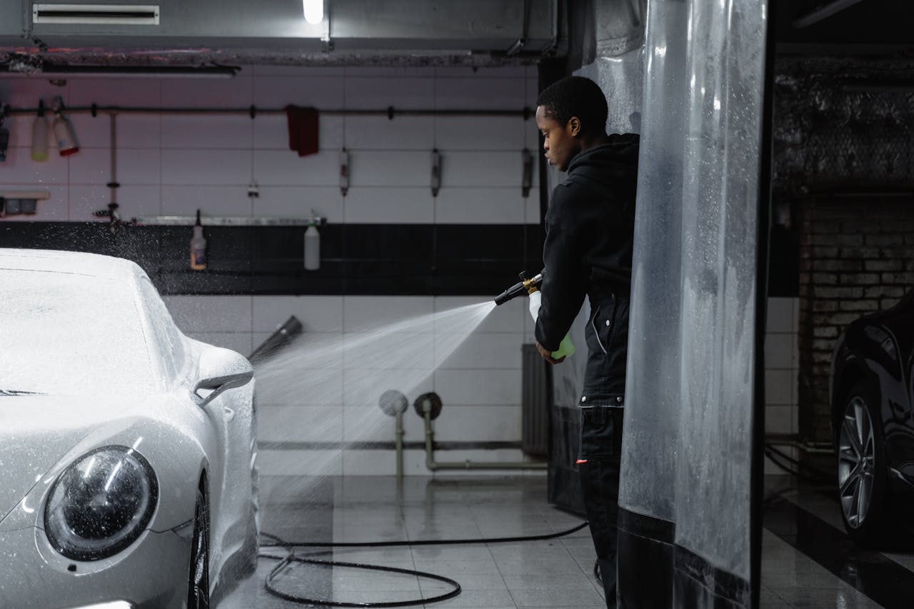 A person using a pressure washer to clean a car in an indoor garage setting.